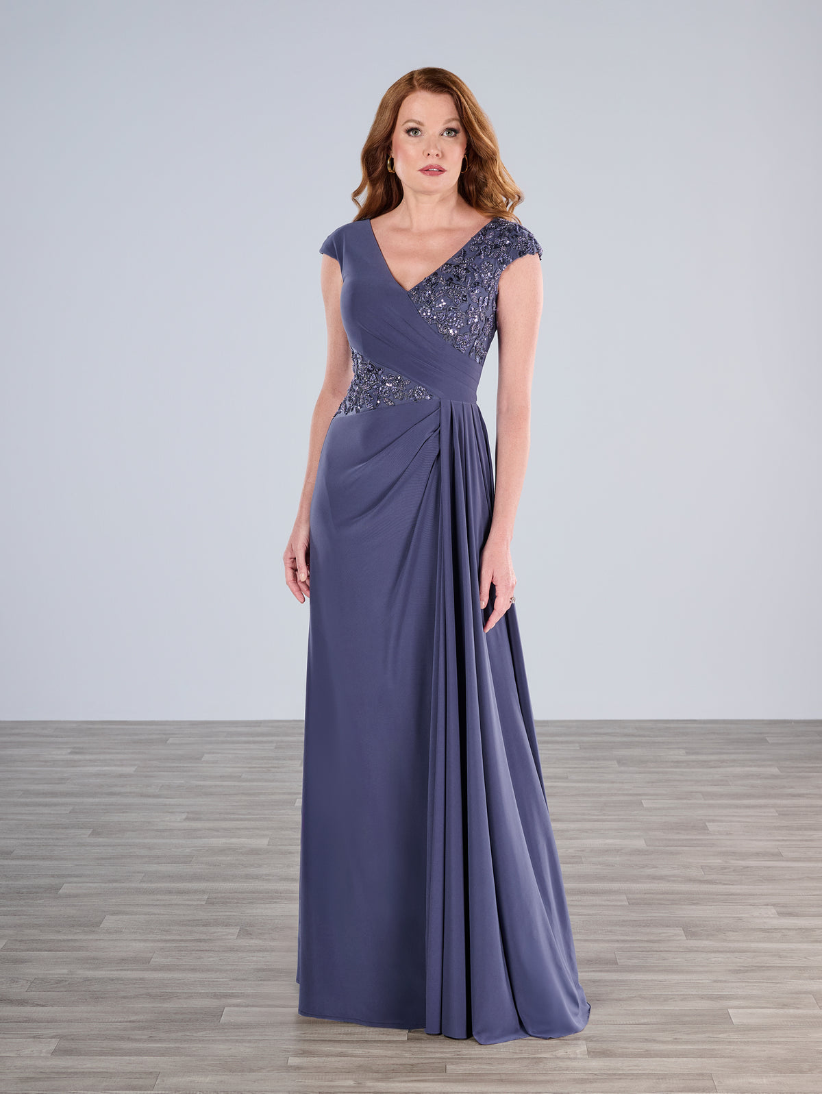 Woman wearing a long purple evening gown with beaded cap sleeves against a plain background / Slim A-line jersey gown features a combination of pleating and beaded lace. V-neck with cup sleeves. Side draping on front skirt.