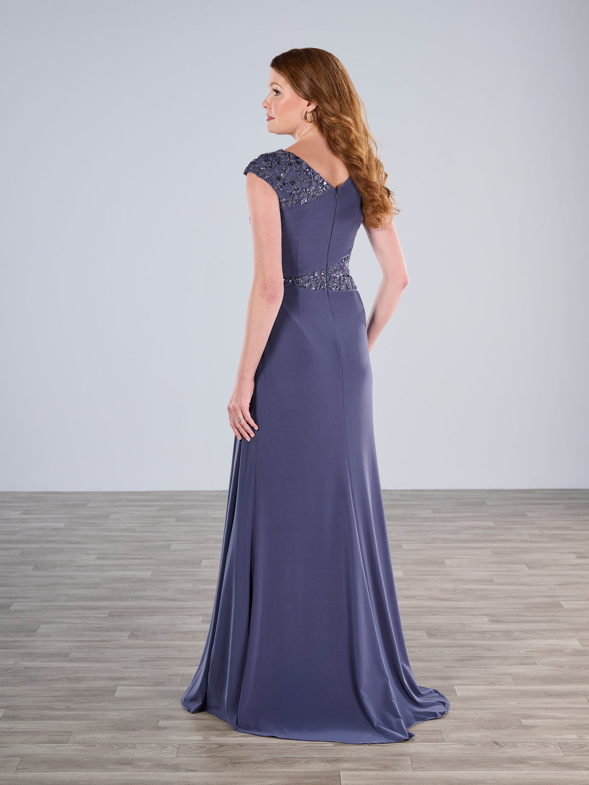 Woman wearing a long purple evening gown with beaded details on a plain background / Slim A-line jersey gown features a combination of pleating and beaded lace. V-neck with cup sleeves. Side draping on front skirt.