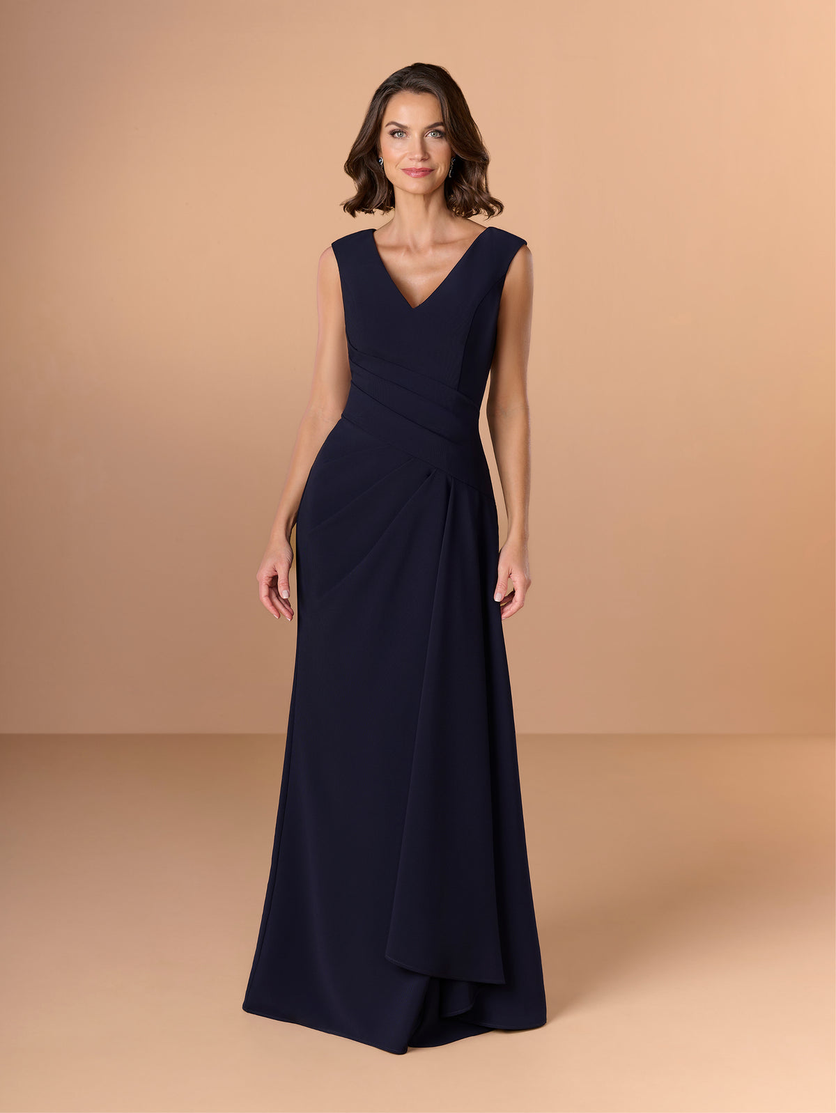 Woman wearing a navy blue evening gown against a beige background / Slim crepe style with V-neck and cup shoulder. Side pleating on front dress with long ruffle on side.