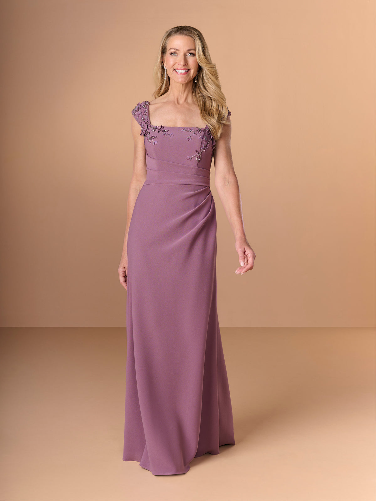 Woman wearing a purple gown with floral details on a beige background / Cap sleeve fitted gown with pleated detail on the bodice and 3D embellishment.