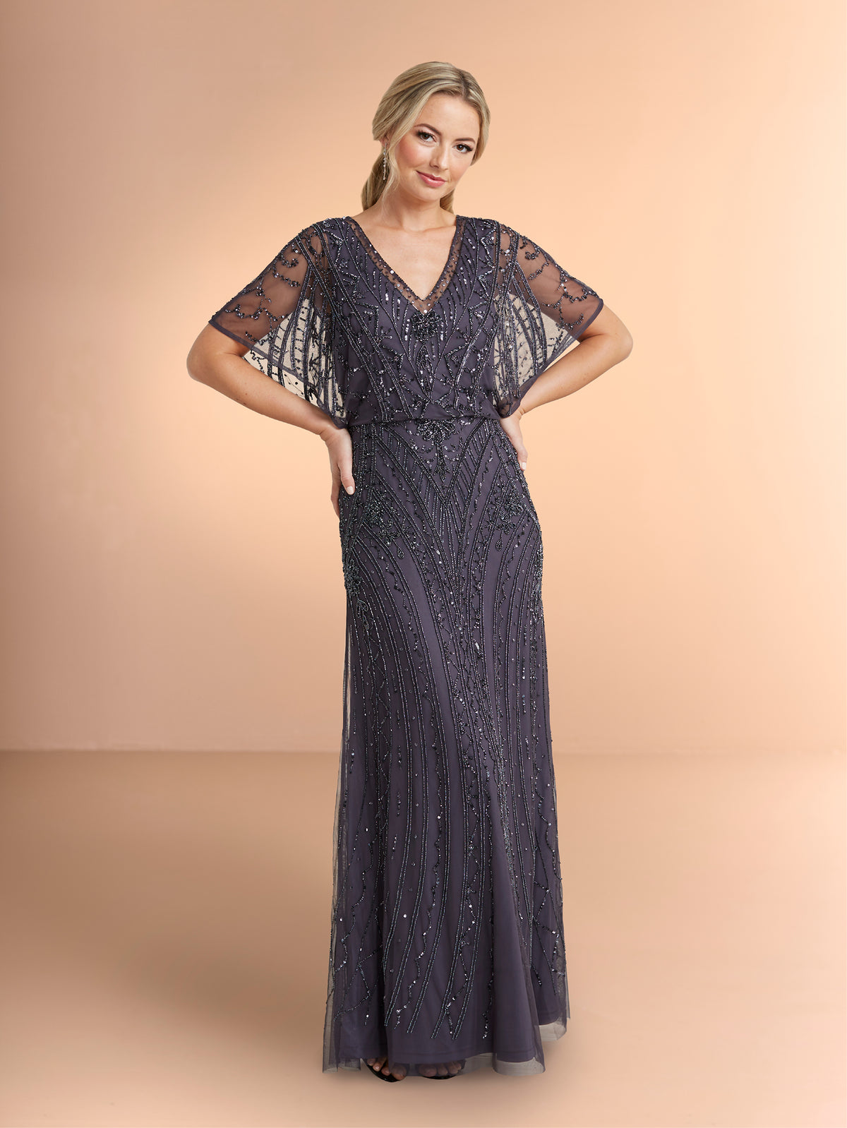 Woman wearing a dark blue evening gown with lace sleeves on a beige background / All over beaded gown with v neckline and long flutter sleeve.