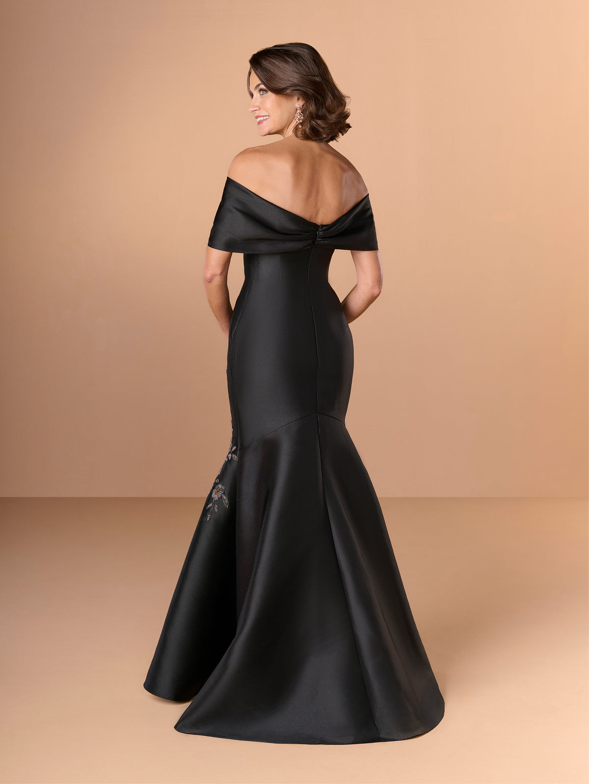 Woman wearing a black off-shoulder gown on a beige background / Off the shoulder mermaid gown with placed beading.