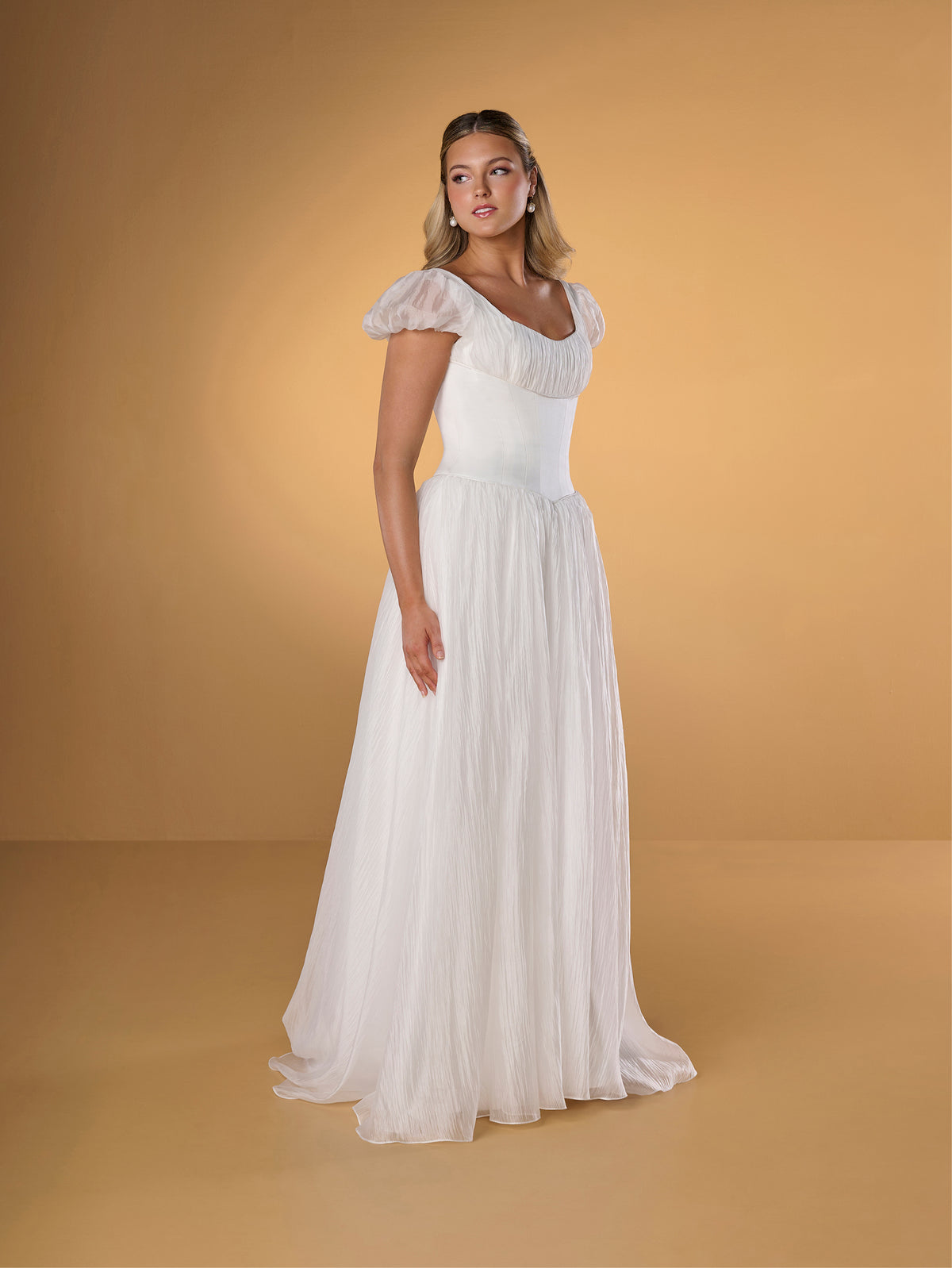 Woman wearing a white dress against a beige background / A-line gown in crinkled organza and satin midriff area on bodice only. Short puffy sleeves. Covered buttons along zipper closure at the back dress.