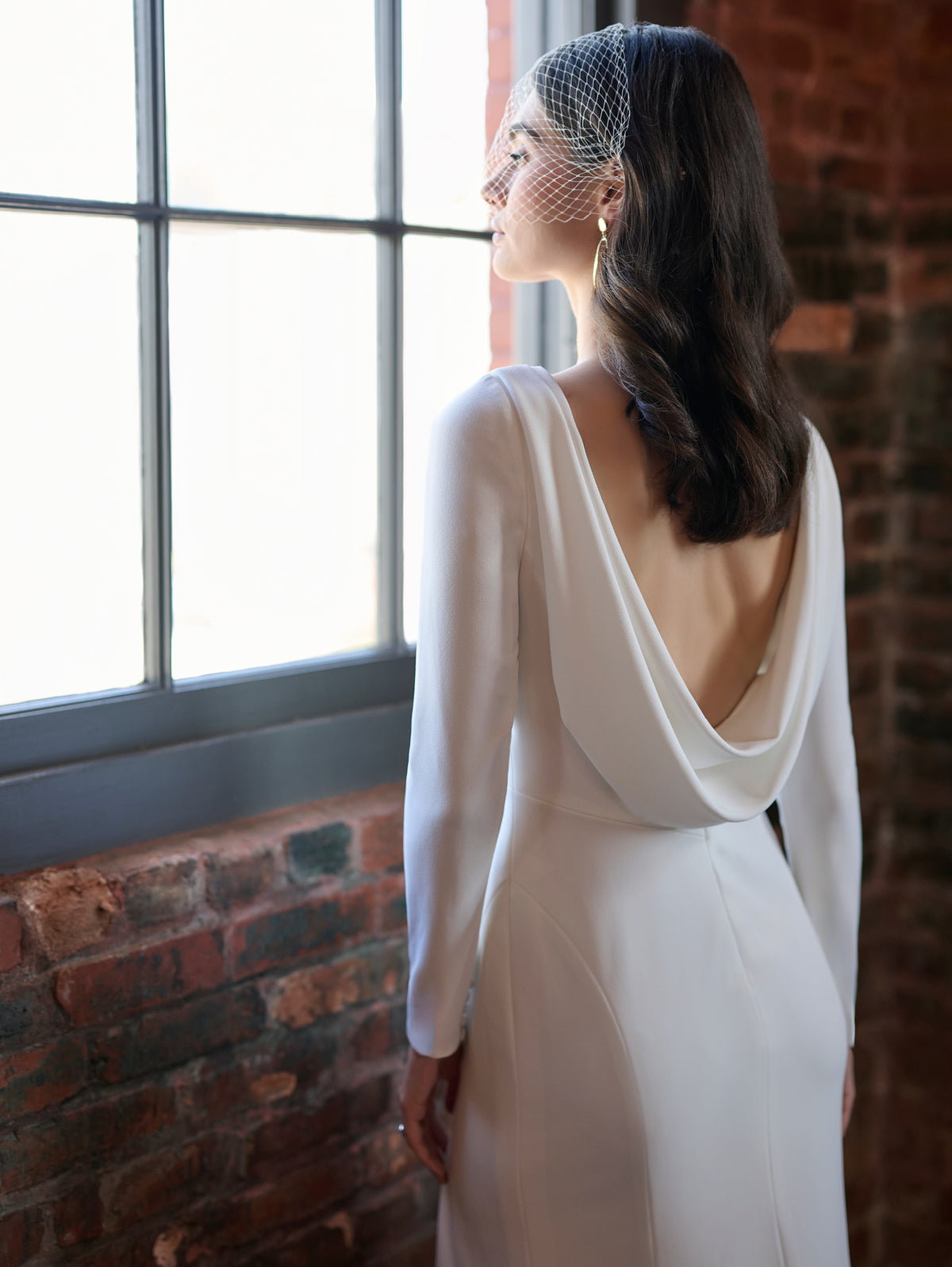This stretch crepe gown features a high neckline with long sleeves and a low cowl back. The fitted skirt has a slit at the front.