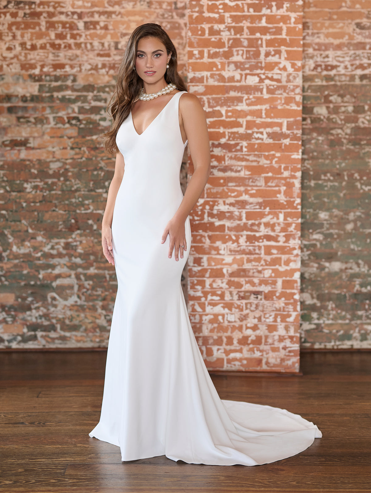 Woman wearing a white gown standing against a brick wall. / This stretch crepe gown has a plunging front neckline and a low, sexy back.