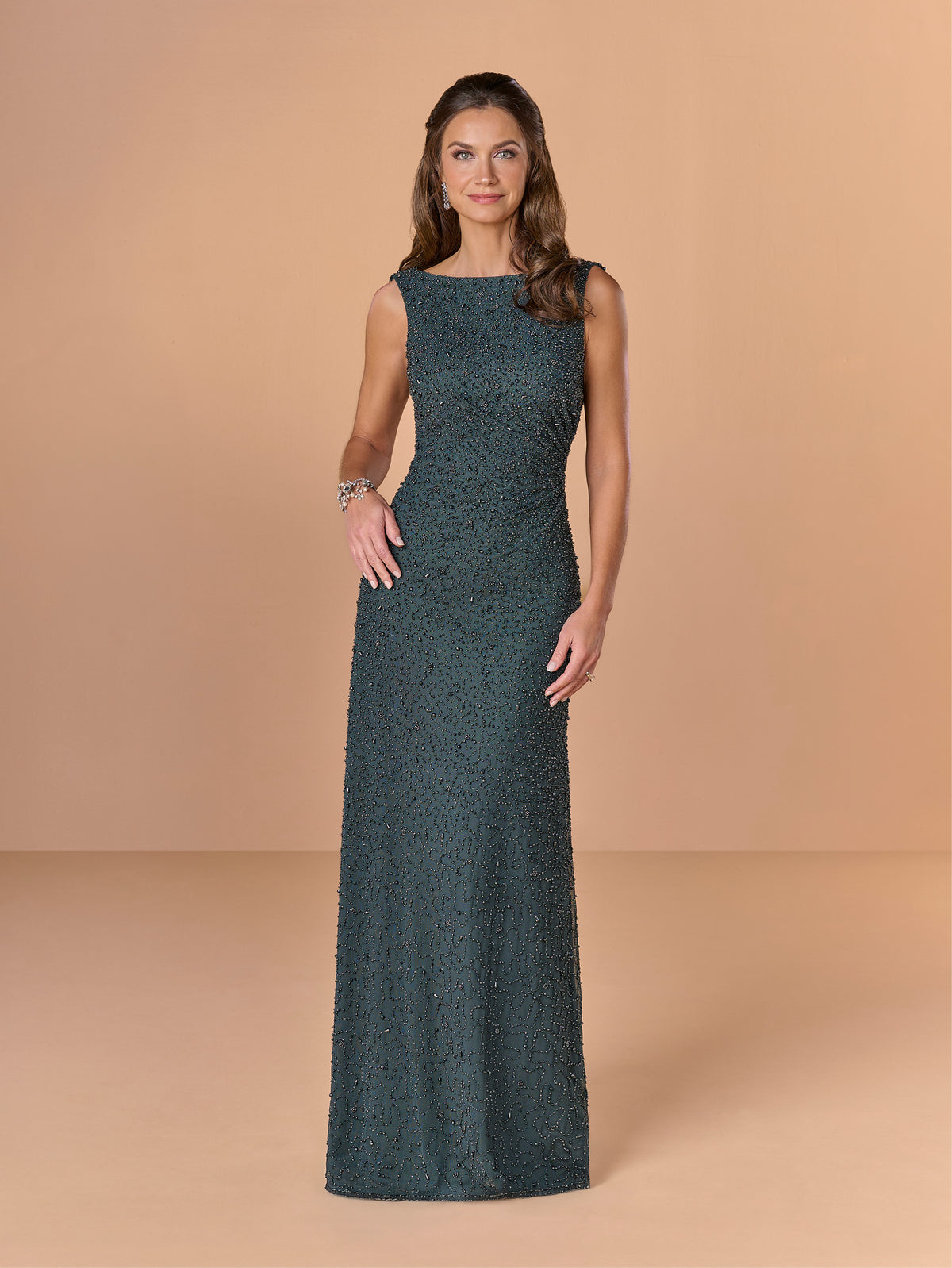 Woman wearing a dark green evening gown against a beige background / All over beaded gown with body shirring and back cowl neckline.
