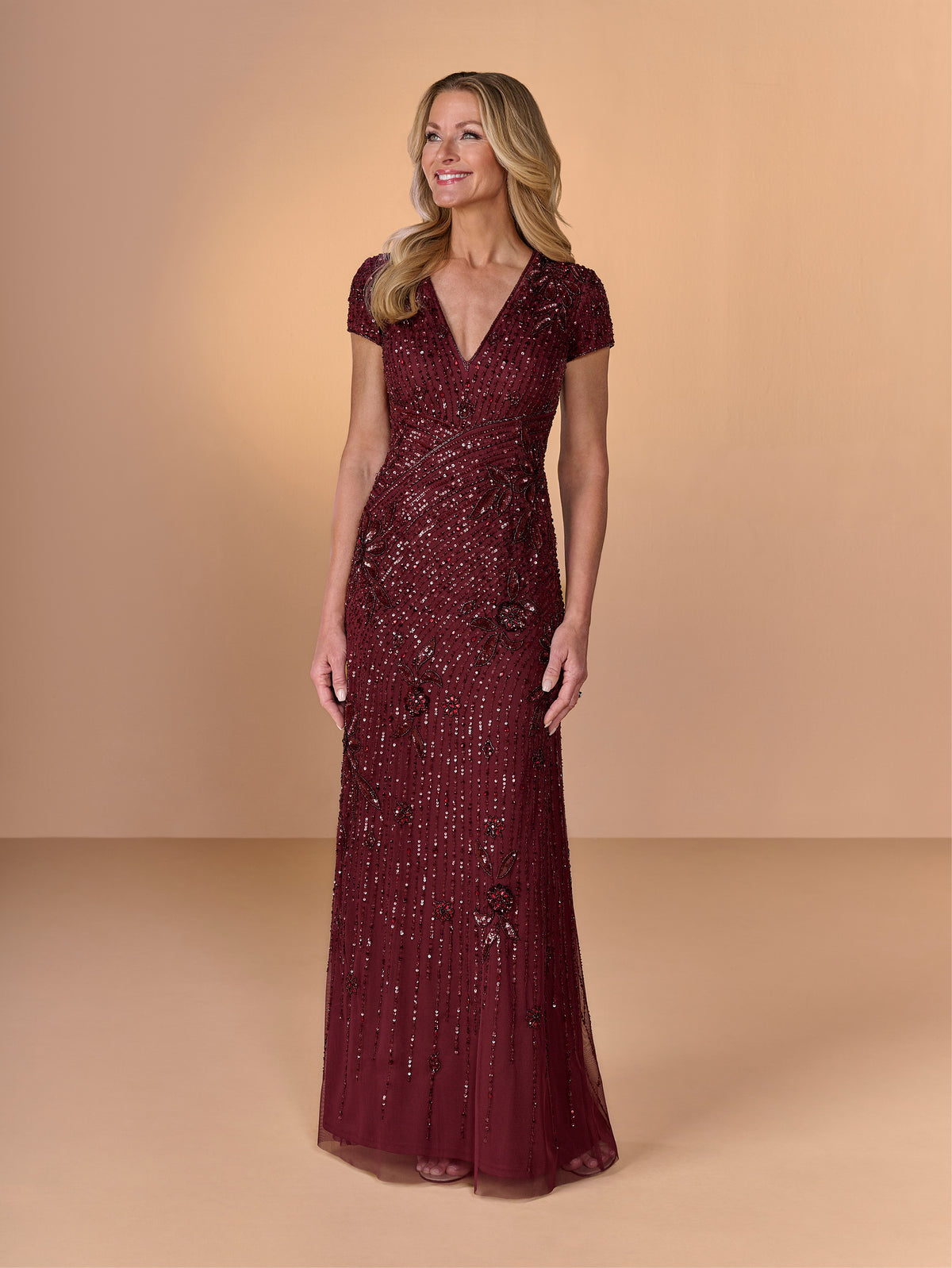 Woman wearing a burgundy sequin dress against a beige background / All over beaded gown with v neckline and cap sleeve.