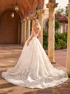 Woman in a white wedding dress standing in an elegant outdoor setting with columns and a building. / Full A-line lace gown with sweetheart neckline. Semi-sheer bodice decorated with 3D motifs and beading. Covered buttons and elastic loops along zipper closure at the back.