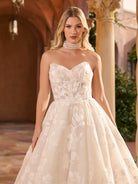 Woman wearing a strapless lace wedding dress in an elegant indoor setting. / Full A-line lace gown with sweetheart neckline. Semi-sheer bodice decorated with 3D motifs and beading. Covered buttons and elastic loops along zipper closure at the back.