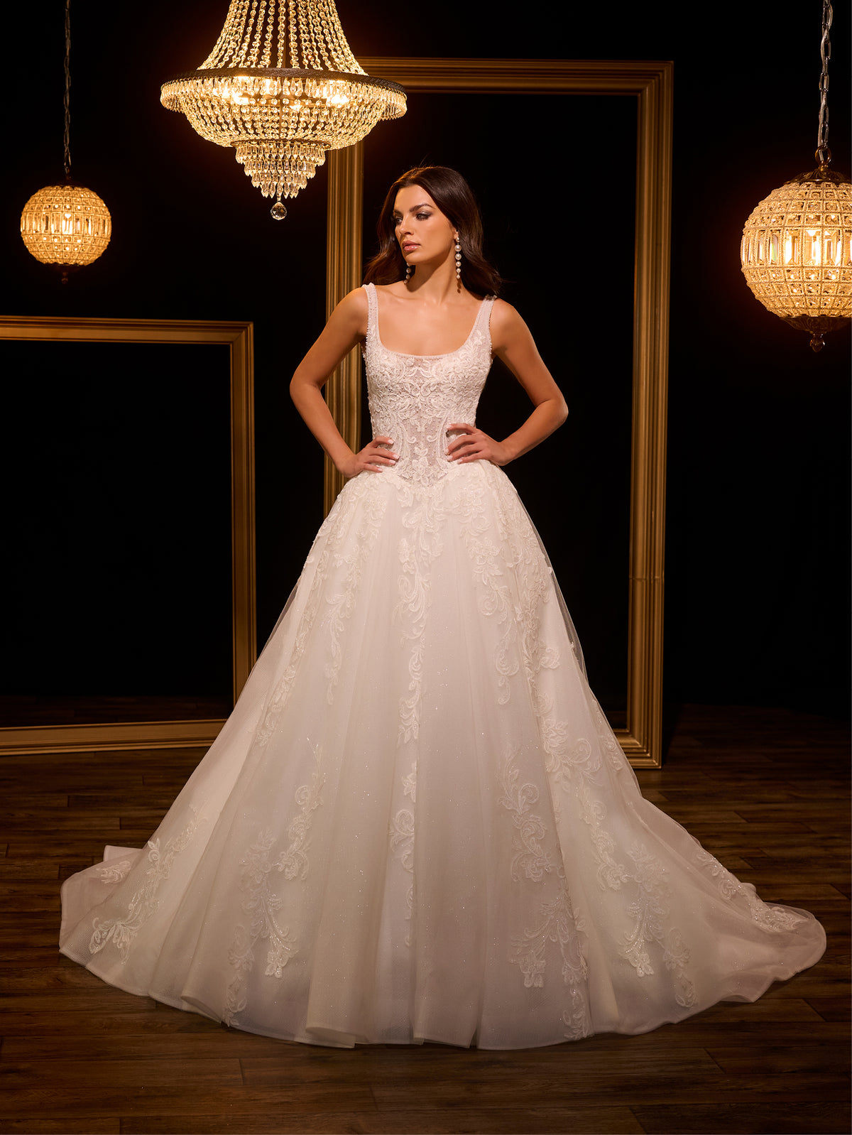 Woman in a white wedding dress standing in a dimly lit room with chandeliers. / Ball gown - shimmer tulle with beaded motifs, square neckline with narrow straps finished with fine beaded trim. Buttons/zipper back closure.