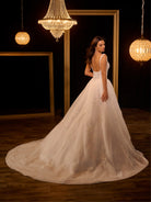 Woman in a white wedding dress standing in a room with chandeliers. / Ball gown - shimmer tulle with beaded motifs, square neckline with narrow straps finished with fine beaded trim. Buttons/zipper back closure.
