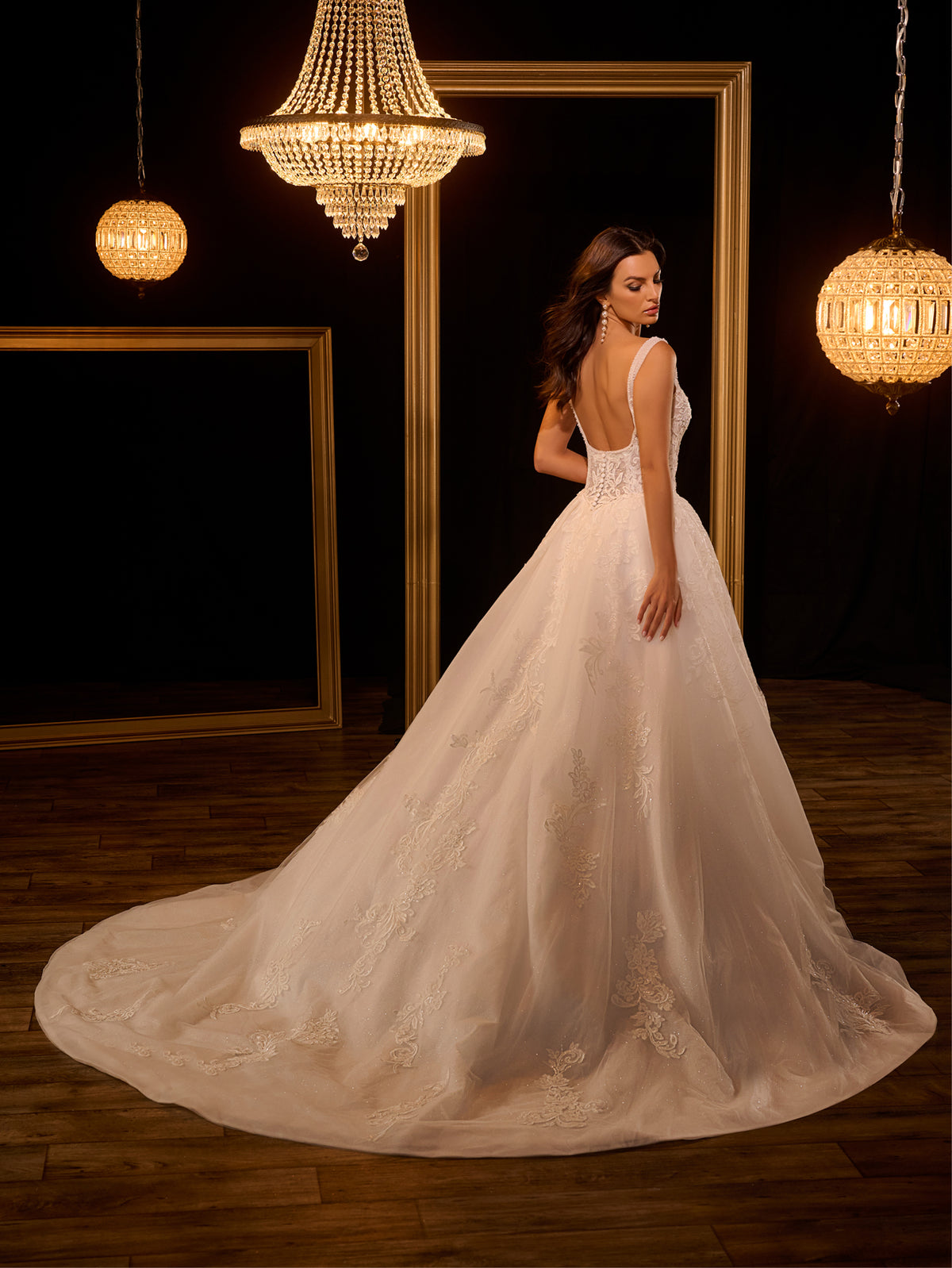 Woman in a white wedding dress standing in a room with chandeliers. / Ball gown - shimmer tulle with beaded motifs, square neckline with narrow straps finished with fine beaded trim. Buttons/zipper back closure.