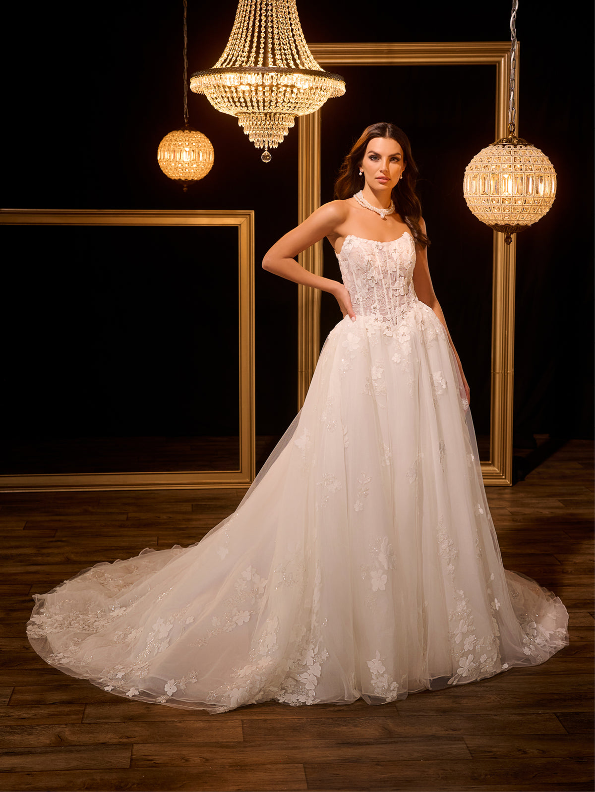 Woman in a white wedding dress standing in a decorated room with chandeliers. / Ball gown with floral lace motifs and split on side skirt.