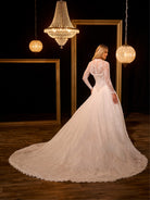 Woman in a white lace wedding dress standing in a room with chandeliers. / Ball gown in all over Chantilly lace with detachable lace bolero. Scooped neckline, buttons/zipper back closure.