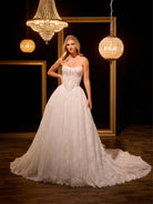 Woman in a white wedding dress standing in a dimly lit room with chandeliers. / Ball gown in all over Chantilly lace with detachable lace bolero. Scooped neckline, buttons/zipper back closure.