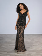 A woman modeling a floor-length black lace evening gown with a V-neckline and sheer mesh overlay, standing on a light gray studio floor against a pale gray background. / Slim style in all over delicate lace with V-neck, decorated with beaded lace motifs. Low scoop back.