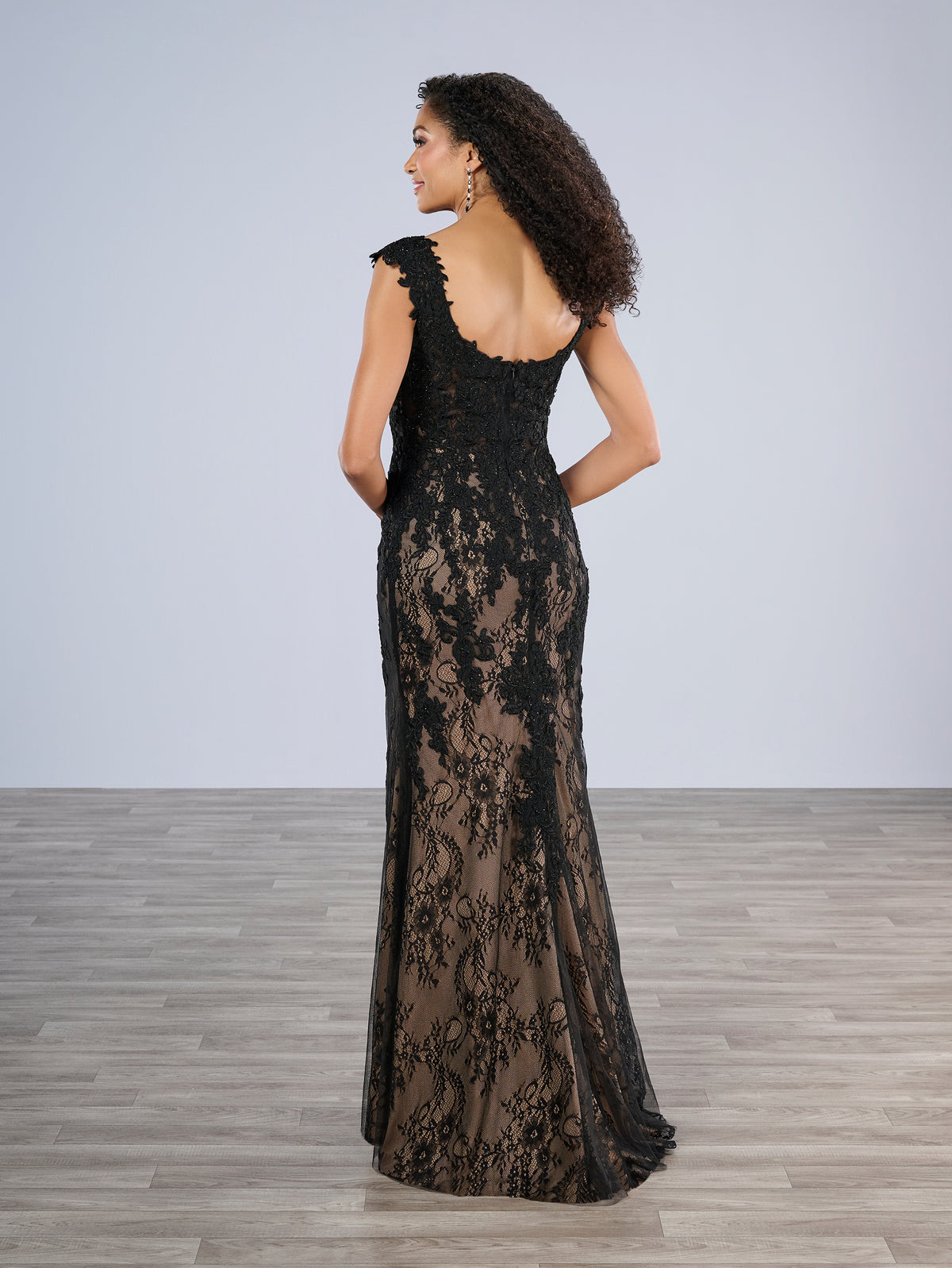 Woman wearing a black lace evening gown against a plain background / Slim style in all over delicate lace with V-neck, decorated with beaded lace motifs. Low scoop back.