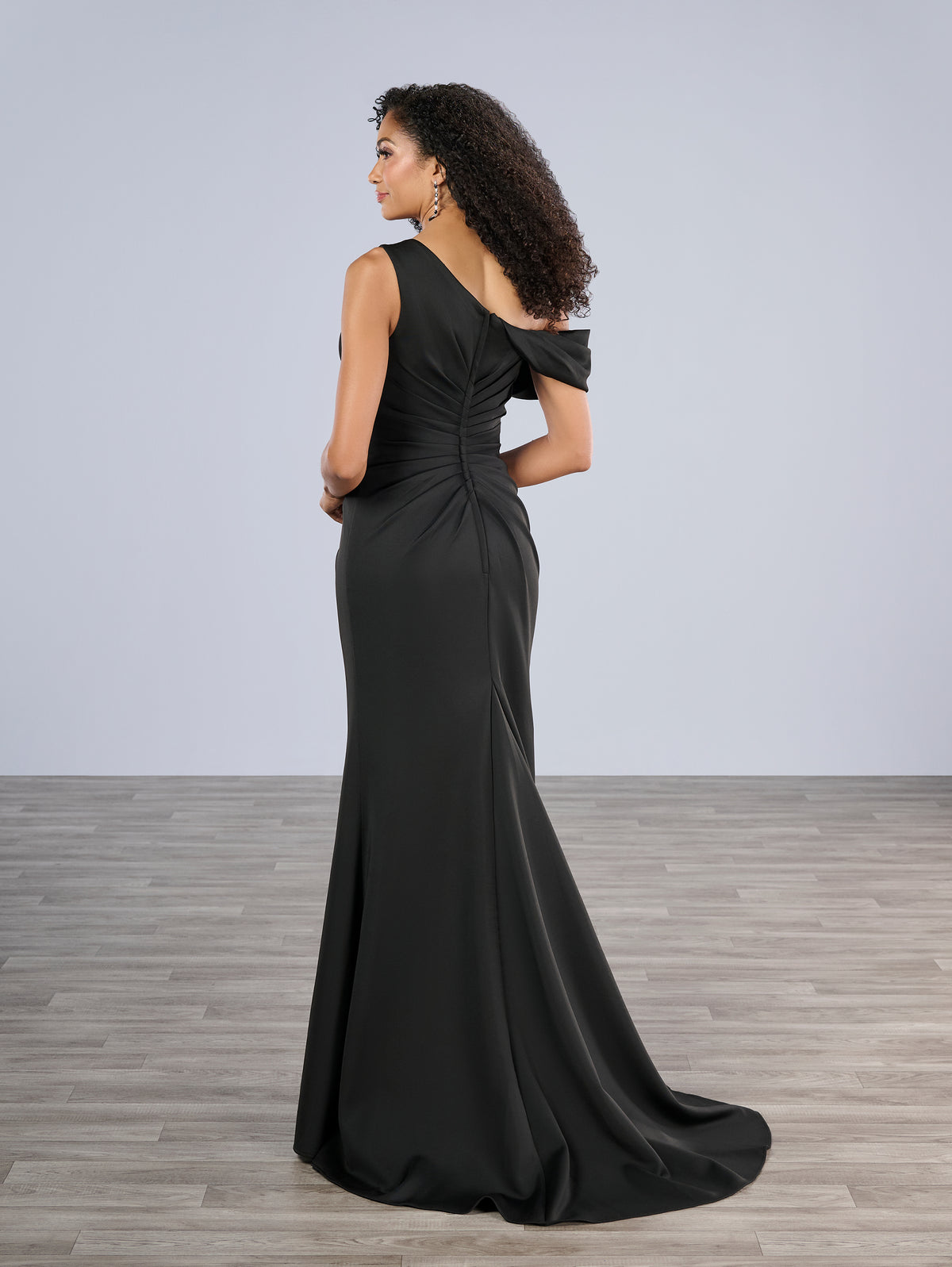 Woman wearing a black evening gown with a plain background / Slim gown with side draping and asymmetrical shoulder and off-shoulder strap on one side. The dress is decorated with beautiful, beaded motifs on the right front side and features a side slit.