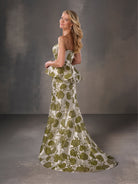 Woman wearing a strapless green and white floral dress against a gray background / Strapless floral brocade peplum fit & flare gown.