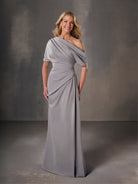 Woman wearing a gray draped gown against a dark background / Stretch charmeuse slim A-line with asymmetrical neckline and off-shoulder sleeve on one side.