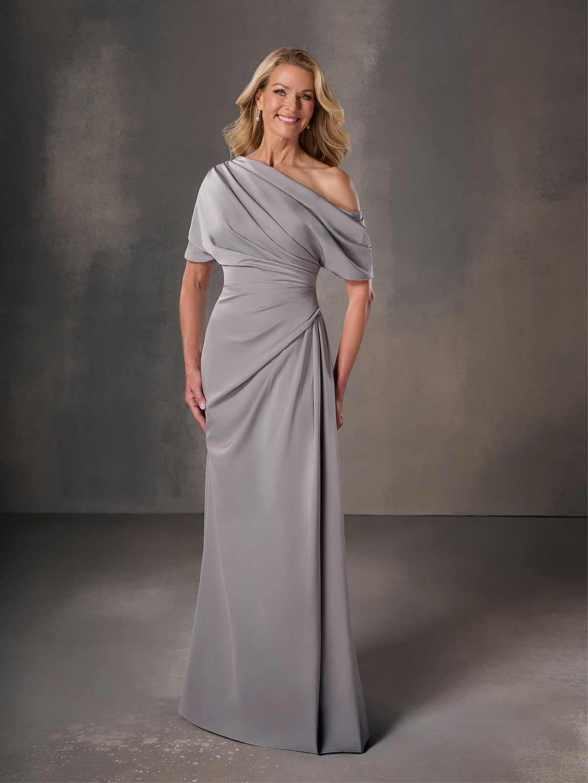 Woman wearing a gray draped gown against a dark background / Stretch charmeuse slim A-line with asymmetrical neckline and off-shoulder sleeve on one side.