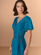Woman wearing a teal dress with embellishments on a beige background / A-line chiffon style with V-neck and short flatter sleeves. Finely gathering on bodice finished with hand beading motif on side waist area.