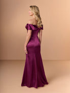 Woman wearing a burgundy off-shoulder gown against a beige background / Slim charmeuse style with straight neckline and off-shoulders collar with twist and bow on side front. Pleating on front dress.