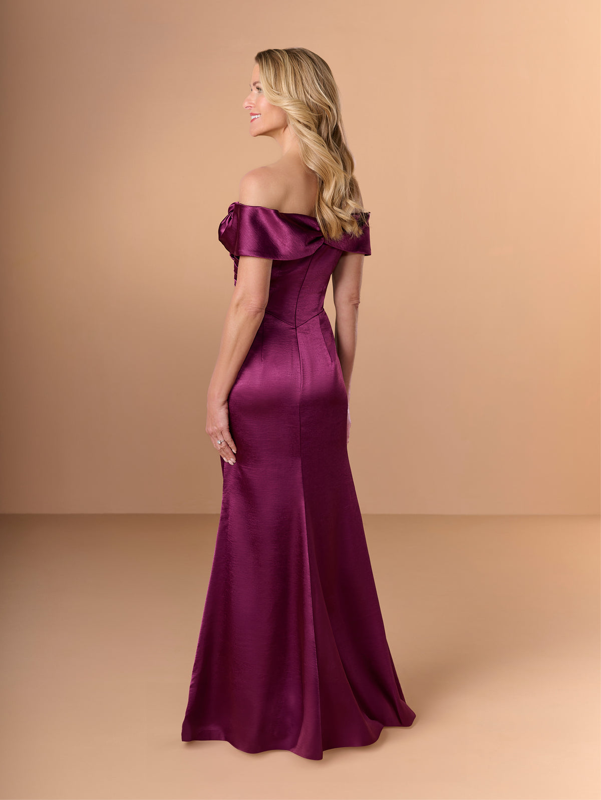 Woman wearing a burgundy off-shoulder gown against a beige background / Slim charmeuse style with straight neckline and off-shoulders collar with twist and bow on side front. Pleating on front dress.