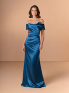 Woman wearing a blue off-shoulder gown against a beige background / Slim charmeuse style with straight neckline and off-shoulders collar with twist and bow on side front. Pleating on front dress.