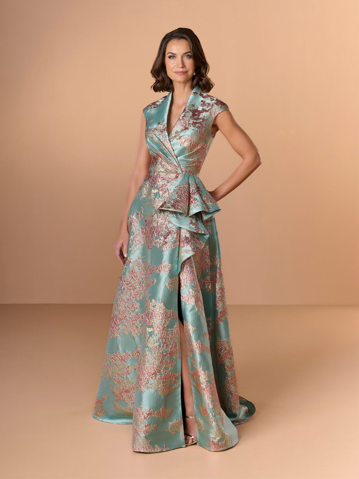 Woman wearing a floral patterned dress on a beige background / A-line style in brocade with V-neck and standing collar at the back neckline. Side front pleating on bodice finished with short ruffle.