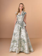 Woman wearing a floral dress against a beige background / A-line style in brocade with V-neck and standing collar at the back neckline. Side front pleating on bodice finished with short ruffle.