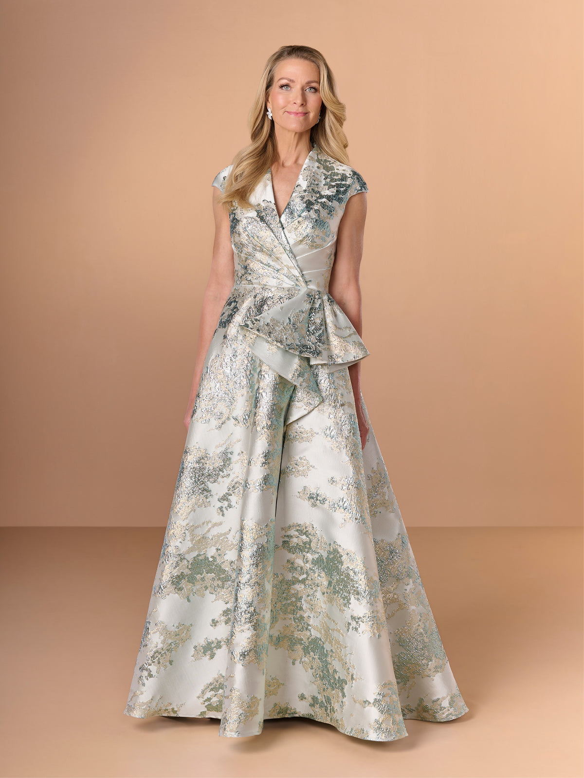 Woman wearing a floral dress against a beige background / A-line style in brocade with V-neck and standing collar at the back neckline. Side front pleating on bodice finished with short ruffle.