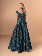 Woman wearing a floral evening gown against a beige background / A-line brocade style with V-neck and short sleeves. Waist band draping with soft bow on side. Invisible zipper closure at the back.