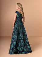Woman wearing a floral jumpsuit on a beige background / A-line brocade style with V-neck and short sleeves. Waist band draping with soft bow on side. Invisible zipper closure at the back.