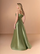 A woman modeling a strapless satin ball gown in sage green, shown from the back against a warm beige studio backdrop. / Slim mikado style with draping on bust area in bow shape going around to the back. Side front draping on stomach area. Detachable back skirt sweep.