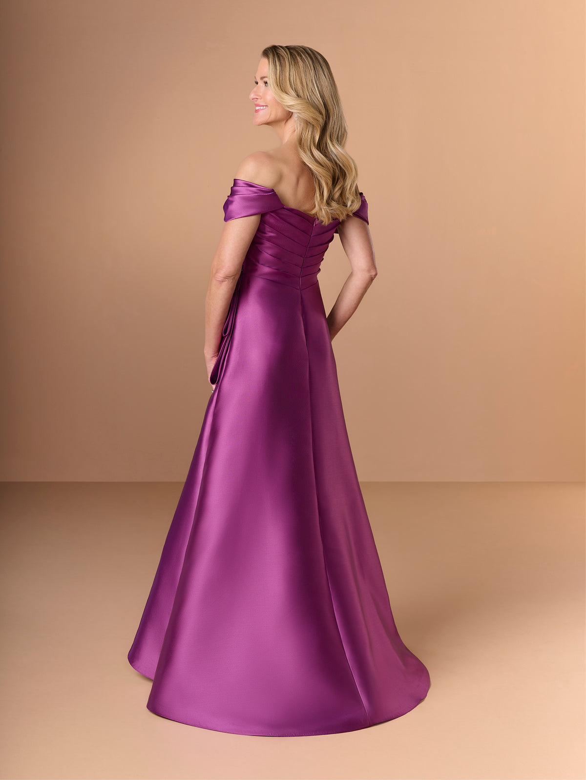 Woman wearing a purple off-shoulder gown against a beige background / A-line mikado style with sweetheart neckline and off-shoulder straps, front draping with bow feature on side.