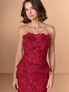 Woman wearing a red strapless lace dress against a beige background / Created with a truly exquisite lace, this strapless gown features a figure-flattering peplum with a stand-away organically cut neckline.