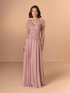 A woman modeling a floor-length dusty pink evening gown with short lace sleeves, a V-neckline, and intricate floral lace applique across the bodice, set against a solid warm beige studio background. / A-line chiffon style with bodice coved with beaded motifs, V-neck short semi sheer sleeves.