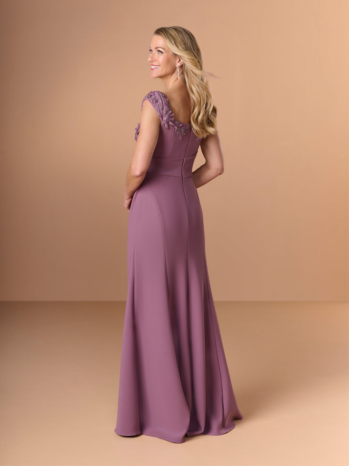 Woman wearing a purple gown with floral details on a beige background / Cap sleeve fitted gown with pleated detail on the bodice and 3D embellishment.