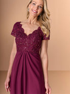 Woman wearing a burgundy evening gown with lace top on a beige background / A-line style with lace bodice and chiffon skirt. V-neck edge and short sleeves hemline edge finished with scallops. Draping on front and back skirt in fan shape.