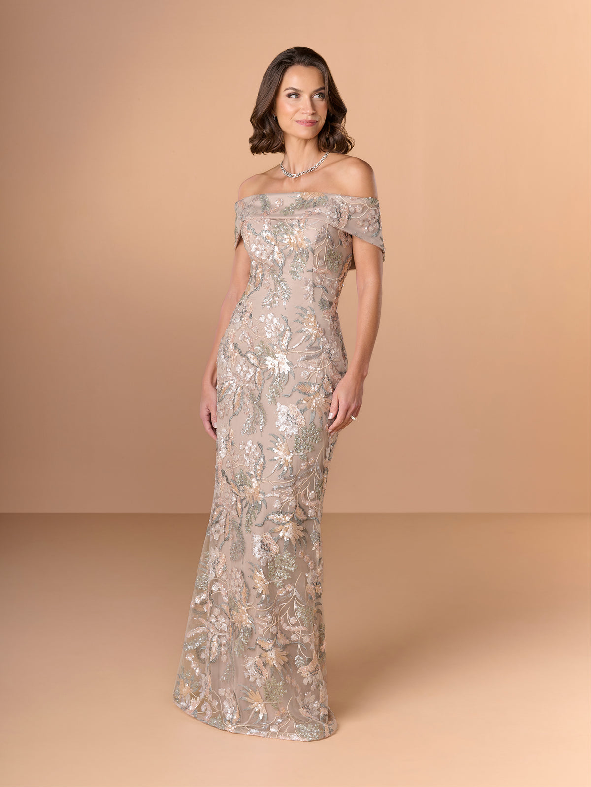 Woman wearing a silver off-shoulder evening gown against a beige background / Slim lace style with straight neckline and wide off shoulder collar. Split on center back skirt.