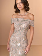 An off-the-shoulder beige evening gown with intricate floral embroidery and sequined detailing, modeled against a solid beige background. / Slim lace style with straight neckline and wide off shoulder collar. Split on center back skirt.