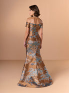 A woman modeling an off-the-shoulder floor-length gown from the back, featuring a brown satin base with a blue and beige floral jacquard pattern, set against a solid beige studio backdrop. / Slim brocade style with sweet off-shoulder neckline, short sleeves, draping on stomach area.