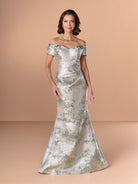 A woman models an off-the-shoulder floor-length gown made of shimmering silver satin with a delicate gold and blue floral pattern, set against a solid beige studio background. / Slim brocade style with sweet off-shoulder neckline, short sleeves, draping on stomach area.