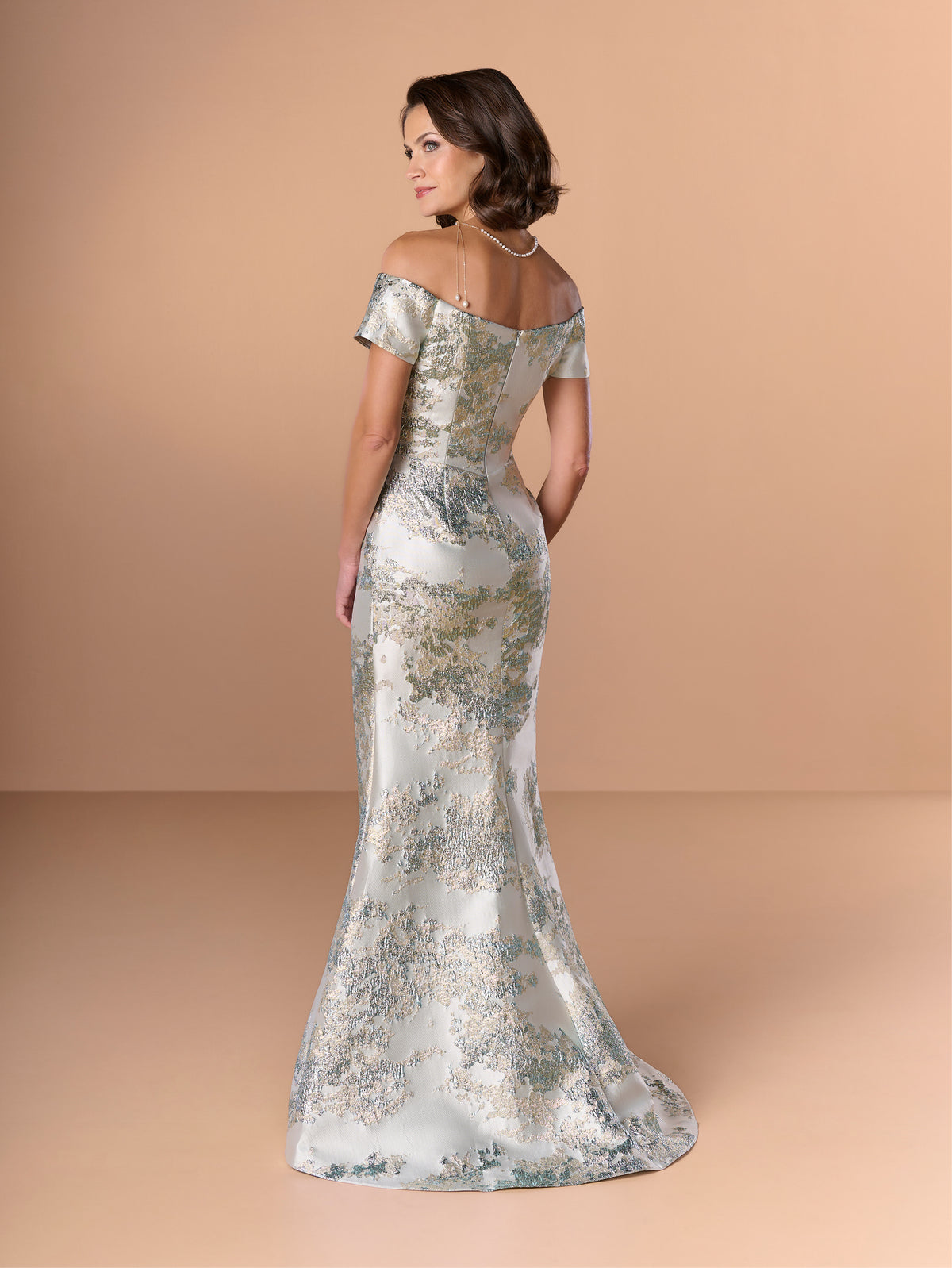 Woman wearing a silver off-shoulder gown against a beige background / Slim brocade style with sweet off-shoulder neckline, short sleeves, draping on stomach area.