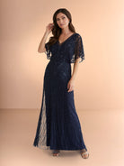 Woman wearing a navy blue evening gown with sheer sleeves against a beige background / All over beaded gown with v neckline and long flutter sleeve.