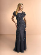 Woman wearing a dark blue evening gown with floral embellishments on a peach background / Slim long beaded style in soft mesh. Rounded neck and sheer short ruffle sleeves. Zipper back closure.