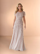 Woman wearing a long, elegant dress with lace details on a beige background / Slim long beaded style in soft mesh. Rounded neck and sheer short ruffle sleeves. Zipper back closure.