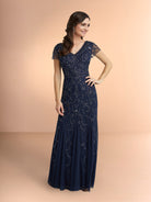 Woman wearing a navy blue lace evening gown on a peach background / Slim long beaded style in soft mesh. V-neck and sheer short sleeves. Zipper back closure.