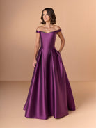 Woman wearing a purple off-shoulder gown against a beige background / Off the shoulder gown with side skirt panels and inserted neckline beading.